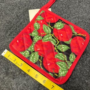 May include: A quilted red and black pot holder with a loop for hanging. The pot holder features a pattern of red apples with green leaves and stems. The border is red. The pot holder measures approximately 8 inches square.