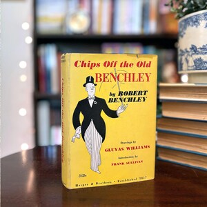 May include: A vintage book titled "Chips Off the Old Benchley" by Robert Benchley. The yellow book cover features an illustration of a man in a tuxedo and top hat. The book is published by Harper & Brothers.
