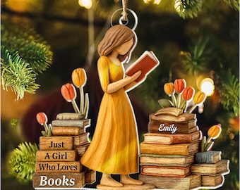 May include: A wooden ornament featuring a woman in a yellow dress reading a book. The ornament has stacks of books with tulips and the text "Just A Girl Who Loves Books" and "Emily". The ornament is hanging from a gold string.