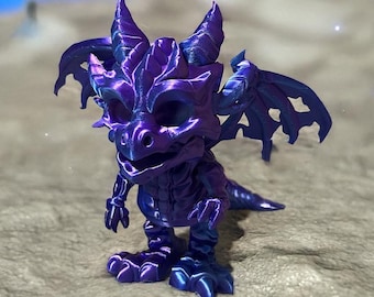 May include: A purple and blue dragon figurine with detailed wings, horns, and claws. The fantasy creature has a smiling expression and is posed on a textured surface. The dragon is a whimsical, decorative item.