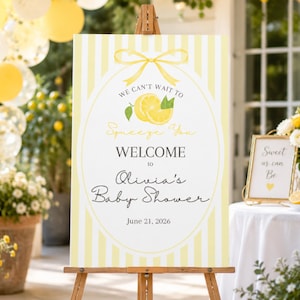 Può includere: Un cartello di benvenuto rettangolare verticale per un baby shower su un cavalletto di legno. Il cartello presenta un bordo a strisce verticali gialle e bianche, una cornice ovale centrale con un fiocco giallo, limoni e il testo We Can't Wait To Squeeze You.