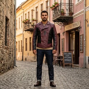 May include: A burgundy leather jacket with black accents and a spider emblem on the chest. The jacket has a quilted design and a classic biker style. The person is wearing blue jeans and brown boots.
