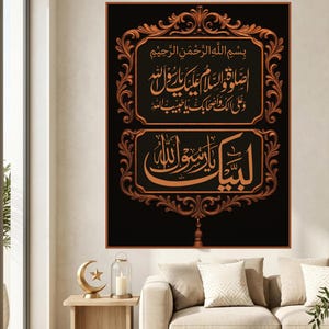 May include: A framed artwork featuring gold Arabic calligraphy on a black background. The frame has an elaborate, swirling design. The artwork is displayed above a beige sofa in a bright room, with a side table.