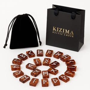 Puede incluir: Un conjunto de piedras rúnicas rectangulares de ámbar báltico con símbolos grabados en color plateado, acompañado de una bolsa de terciopelo negro con cordón y una bolsa de regalo negra con el texto KIZIMA BALTIC AMBER impreso en oro.