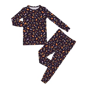 May include: A two-piece pajama set featuring a dark purple background with a repeating pattern of gold and white religious symbols. The long-sleeved top and matching pants are made of a soft material, perfect for a comfortable night's sleep.