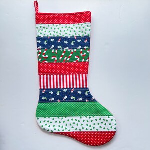 May include: A red, green, white, and blue Christmas stocking with a variety of patterns, including polka dots, stripes, and snowflakes. The stocking is quilted and has a loop at the top for hanging.