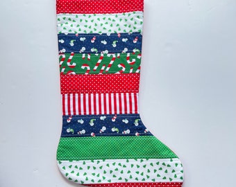 May include: A red, green, white, and blue Christmas stocking with a variety of patterns, including polka dots, stripes, and snowflakes. The stocking is quilted and has a loop at the top for hanging.