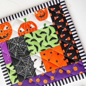 May include: A quilted Halloween-themed hot pad with a patchwork design featuring pumpkins, bats, candy corn, and spiderwebs. The hot pad is bordered with black and white stripes.