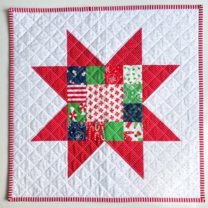 May include: A quilted Christmas-themed table topper featuring a large red star with white polka dots. The star's center is composed of smaller squares with festive patterns. The border is white with a red and white striped edge.