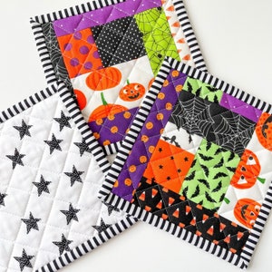 May include: Three Halloween-themed quilted pot holders. One is white with black stars, one is purple, black, and green with a spiderweb, bats, and pumpkins, and one is black, white, and orange with a variety of Halloween patterns.