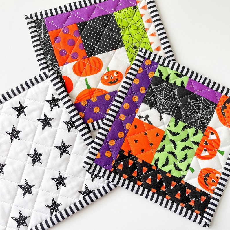 May include: Three Halloween-themed quilted pot holders. One is white with black stars, one is purple, black, and green with a spiderweb, bats, and pumpkins, and one is black, white, and orange with a variety of Halloween patterns.