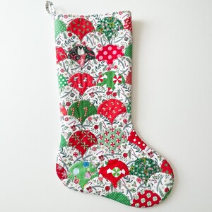 May include: A handmade Christmas stocking with a patchwork design. The stocking features a variety of red, green, and white patterned fabrics, including polka dots, candy canes, and floral prints. A loop is attached for hanging.