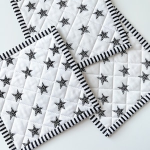 May include: Three white quilted pot holders with black star patterns and black and white striped borders.