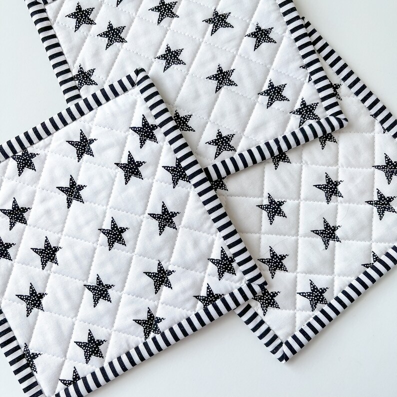 May include: Three white quilted pot holders with black star patterns and black and white striped borders.