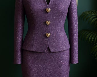 May include: A purple tweed skirt suit displayed on a mannequin. The suit features a fitted blazer with heart-shaped gold buttons and a matching knee-length skirt. The fabric has a subtle sparkle, and the suit is set against a dark green background.