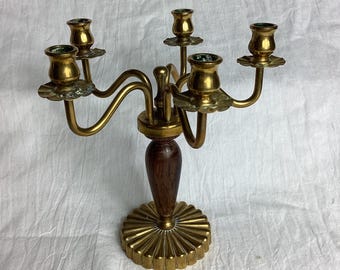 May include: A five-arm candelabra featuring a polished brass finish with a central dark wood stem. The base is circular with a fluted, sunburst-like design, and each of the five candle holders is supported by curved brass arms extending outward.