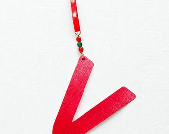 May include: A bright red wooden bookmark in a V-shape, with a red ribbon and small green and red beads. The bookmark is designed to be inserted into a book. The background is white.