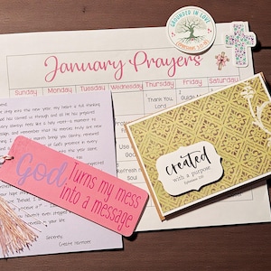 Puede incluir: Una colección de artículos de papelería que incluyen un marcapáginas rosa con el texto "God Turns my mess into a message", un calendario, una tarjeta con el texto "created with a purpose" y una carta.