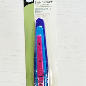 May include: Package of Dritz brand elastic threaders in blue and pink. The package includes three threaders for 1/4", 1/2", and 3/4" widths. The package also includes the text "Elastic Threaders" and "Enhebradores de Elástico".