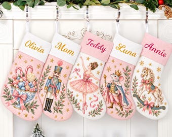 May include: Five personalized Christmas stockings in shades of pink and white, each featuring a unique holiday illustration including a nutcracker, a ballerina, a mouse king, a rocking horse, and a bowl of candy, with names embroidered on the cuffs.