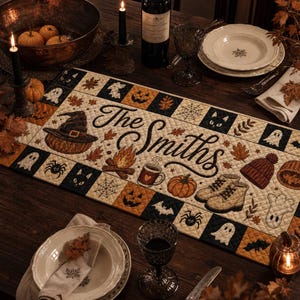 Pode incluir: Um caminho de mesa retangular acolchoado com o texto The Smiths em letra cursiva preta, rodeado por ilustrações de abóboras, um chapéu de bruxa, fantasmas, aranhas, gatos, uma fogueira, uma caneca, botas e um gorro em tons de laranja, preto e creme.