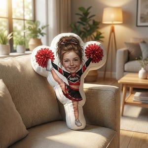 May include: A custom-shaped pillow featuring a cartoon illustration of a cheerleader in a red, black, and white uniform. The cheerleader is holding red pom-poms and has the name "Sophia" on the uniform. The pillow is on a beige sofa.