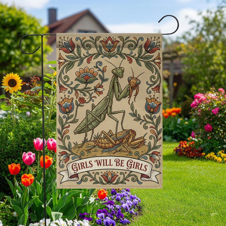 May include: A beige garden flag featuring a detailed illustration of a praying mantis with a floral border. The mantis is depicted with another insect, and the text "GIRLS WILL BE GIRLS" is displayed on a banner.