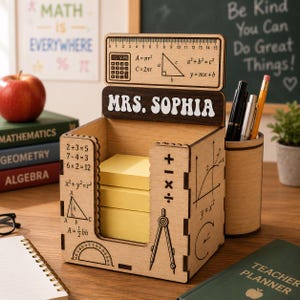 May include: A light-colored wooden desk organizer featuring the name MRS. SOPHIA, a 15 cm ruler, mathematical formulas, and geometric illustrations. The box holds a stack of yellow sticky notes and includes a cylindrical pen holder attachment.