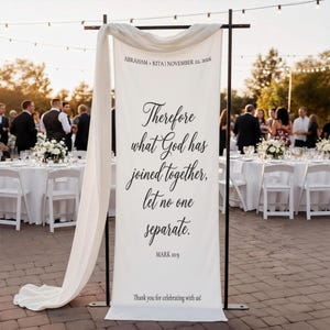 Könnte beinhalten: Ein weißes Banner mit schwarzem Text, das bei einer Outdoor-Veranstaltung angezeigt wird. Auf dem Banner steht "Darum, was Gott zusammengefügt hat, soll der Mensch nicht scheiden" und enthält die Namen "Abraham + Rita" und das Datum "22. November 2026".