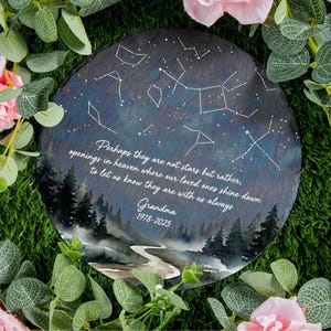 May include: A round, dark gray memorial stone with a painted night sky design and constellations. The stone features a watercolor landscape and a heartfelt quote, with the name "Grandma" and dates.