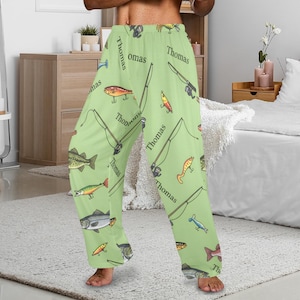May include: Light green pajama pants with a repeating pattern of fishing rods, lures, and various fish. The word "Thomas" is printed vertically on the pants. These comfortable pants are perfect for lounging or sleeping.