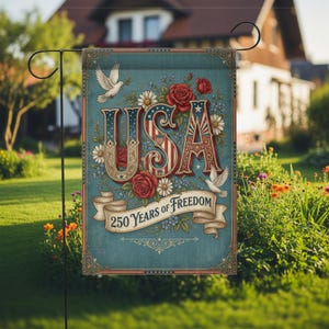 Op de afbeelding: Een tuinvaandel met het woord "USA" in een patriottisch ontwerp, omringd door rode rozen, witte madeliefjes en duiven. De vlag leest "250 Years of Freedom" op een banner. De vlag wordt in een tuin getoond.