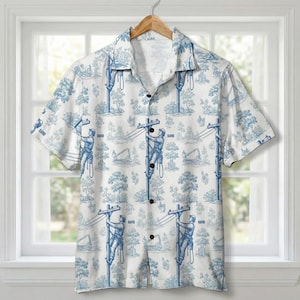 Op de afbeelding: Korte mouwen button-down shirt met een witte achtergrond en een blauw toile de Jouy patroon met nutsarbeiders op telefoonpalen, bomen en bouwmachines. Het shirt hangt aan een houten hanger.