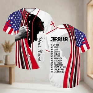 Könnte beinhalten: Weißes Baseball-Trikot mit roten und blauen Akzenten, mit einem Design der amerikanischen Flagge auf den Ärmeln. Das Trikot enthält den Text "JESUS" und eine Liste von Attributen. Auf der Vorderseite steht der Text "Your Name" und eine Silhouette.
