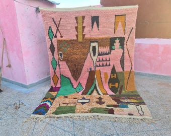 May include: A pink, geometric patterned rug with a variety of shapes and colors. The rug features brown, green, yellow, and blue accents. The rug has a fringe along the bottom edge.