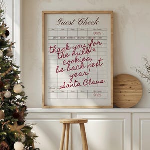May include: A framed print with a grid design, resembling a guest check, features the text "Guest Check" at the top. Handwritten in red script are the words "thank you for the milk & cookies, be back next year! Santa Claus."