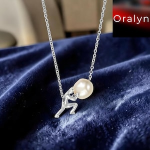 May include: A silver-toned necklace featuring a pendant shaped like a figure pushing a round, cream-coloured pearl. The chain is a delicate link style. The word Oralyn is printed in white text in the upper right corner of the image frame.