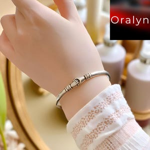 以下が含まれることがあります： 握手をした形をした留め金が付いたシルバーカラーのブレスレット。 ブレスレットはシンプルでエレガントなデザインで、普段使いに最適です。 留め金にはエッチングされた線が施されており、視覚的な魅力を高めています。