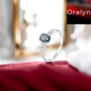 Peut inclure: Une bague en argent ornée d'une grosse pierre précieuse ovale de couleur teal. La bague présente des feuilles délicates et de petits diamants sur le bandeau. La bague est présentée sur une surface en velours rouge.