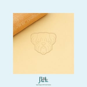 Könnte beinhalten: Ein hellbrauner Ausstecher in Hundeform mit einer Teigrolle im Hintergrund. Der Ausstecher ist eine Strichzeichnung eines Hundegesichts. Das Bild hat einen hellblauen Hintergrund. Der Text "J Cutters" steht unten.