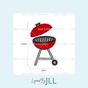 Può includere: Un barbecue rosso con griglia nera e coperchio incernierato. Il barbecue è alto 10,3 cm e largo 6,6 cm. Ha gambe grigie e una ruota. Il testo "Just Little Luxuries" è ripetuto nell'immagine.