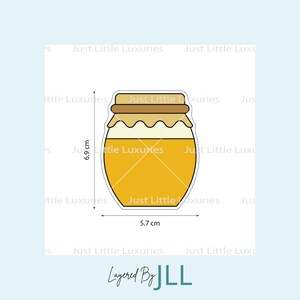 Könnte beinhalten: Cartoon-Illustration eines Honigglases, gefüllt mit goldenem Honig. Das Glas ist 6,9 cm hoch und 5,7 cm breit. Es hat einen braunen Deckel und ein weißes Etikett. Der Text "Just Little Luxuries" wiederholt sich um das Glas.