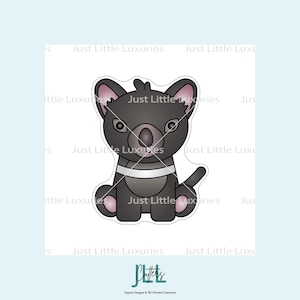 May include: A cartoon-style cookie cutter in the shape of a Tasmanian devil. The cutter is black with pink accents on the ears, paws, and nose. It has a white stripe across the chest and the text "Just Little Luxuries" is visible.