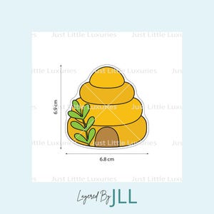 May include: A yellow beehive-shaped design with a brown entrance and green leaves. The design is 6.8 cm wide and 6.9 cm tall. The text "Layered By JLL" is at the bottom.
