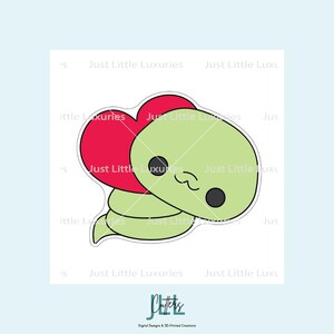 Könnte beinhalten: Eine niedliche Cartoon-Schlange mit einem roten Herzen. Die Schlange ist hellgrün mit schwarzen Augen und einem lächelnden Mund. Das Bild enthält den Text "Just Little Luxuries" und "Chatters" unten.