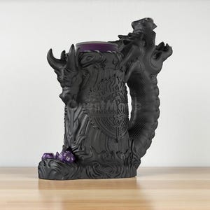 May include: A black dragon-themed dice tower with a purple interior and a dragon figure on the side. The tower has the text "DRAGON STAIR" on the front and a few purple dice at the base. The tower is on a wooden surface.