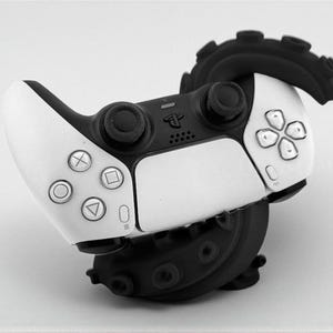 May include: A white and black PlayStation 5 controller with a black octopus-like base. The controller has the standard button layout with a directional pad, face buttons, and analog sticks. The octopus base adds a unique design.