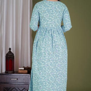 K&ouml;nnte beinhalten: Hellblaues Maxikleid mit floralem Muster und Dreiviertel&auml;rmeln. Das Kleid hat eine geraffte Taille und einen Schlitz am Saum. Das Blumenmuster enth&auml;lt wei&szlig;e und violette Akzente.
