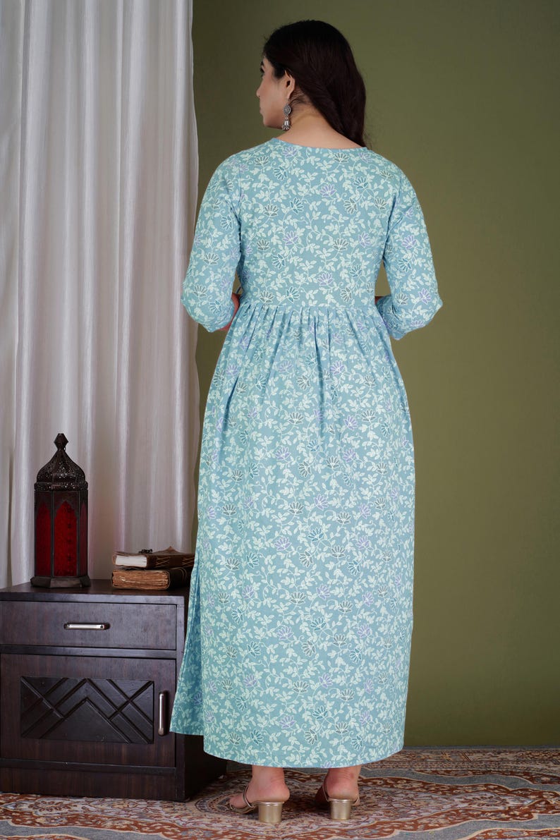 K&ouml;nnte beinhalten: Hellblaues Maxikleid mit floralem Muster und Dreiviertel&auml;rmeln. Das Kleid hat eine geraffte Taille und einen Schlitz am Saum. Das Blumenmuster enth&auml;lt wei&szlig;e und violette Akzente.
