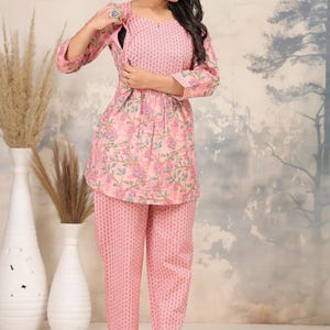 May include: A two-piece pink floral print outfit. The top has a round neckline and three-quarter sleeves. The pants are a matching pink print. The outfit is suitable for casual wear.